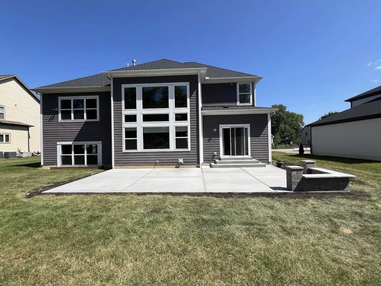 Front view of a modern gray two-story house with large white-trimmed windows, a concrete patio, and steps at the entry.