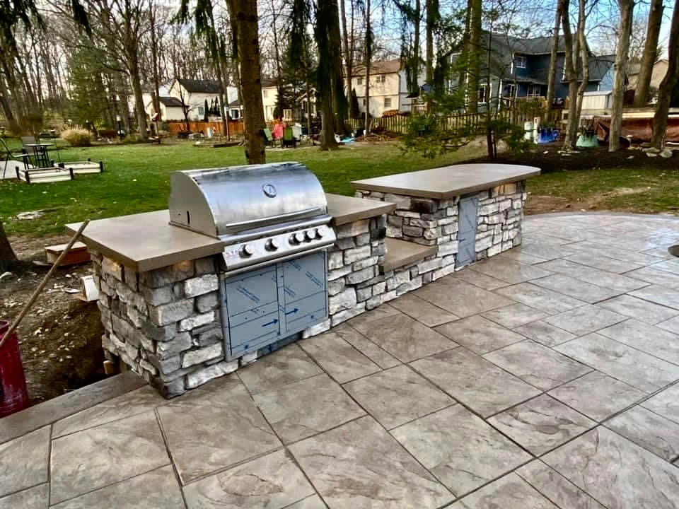Outdoor stone-built barbecue island with a stainless steel grill and granite countertops on a paved patio in a backyard park setting: perfect for outdoor cooking and entertaining.