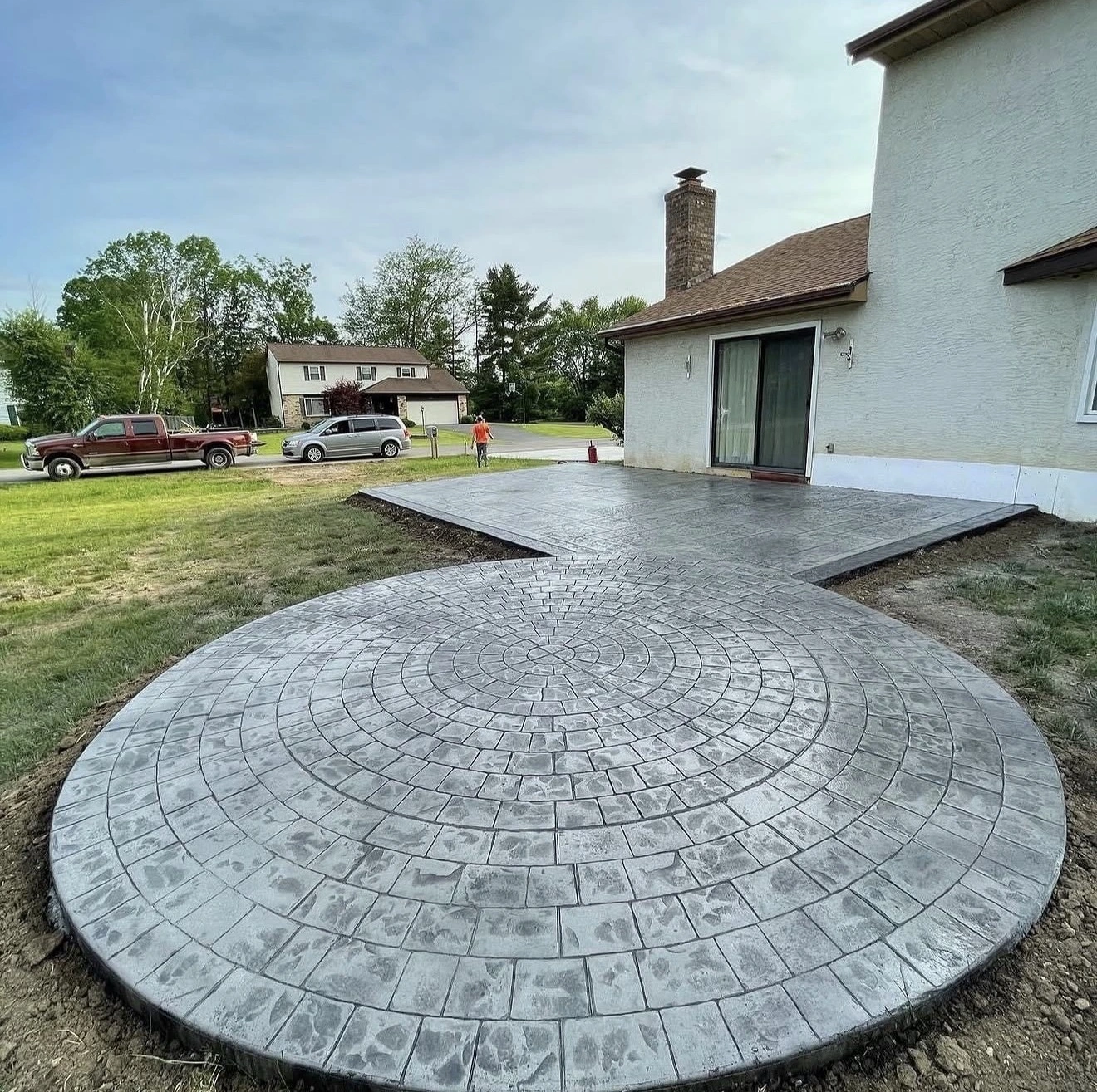 Circular stamped concrete patio in the backyard, with a curved circular pattern extending from the house toward the lawn and driveway.