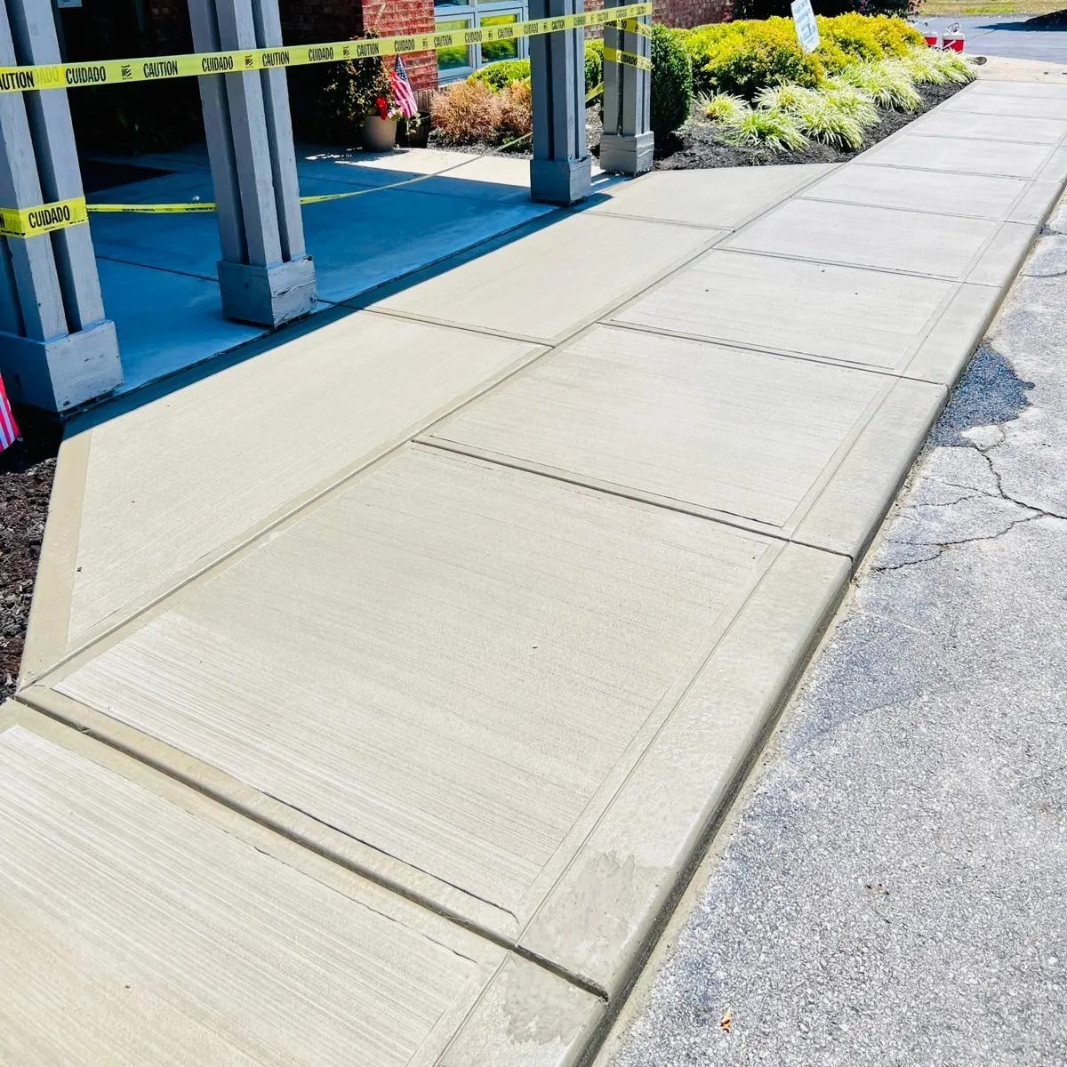 Freshly poured concrete sidewalk panels along a storefront with yellow caution tape in the background.