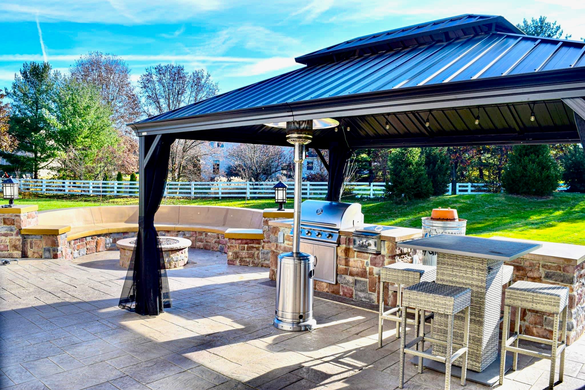 Outdoor patio with a metal gazebo, built-in grill, and stone seating area under a blue metal roofed canopy