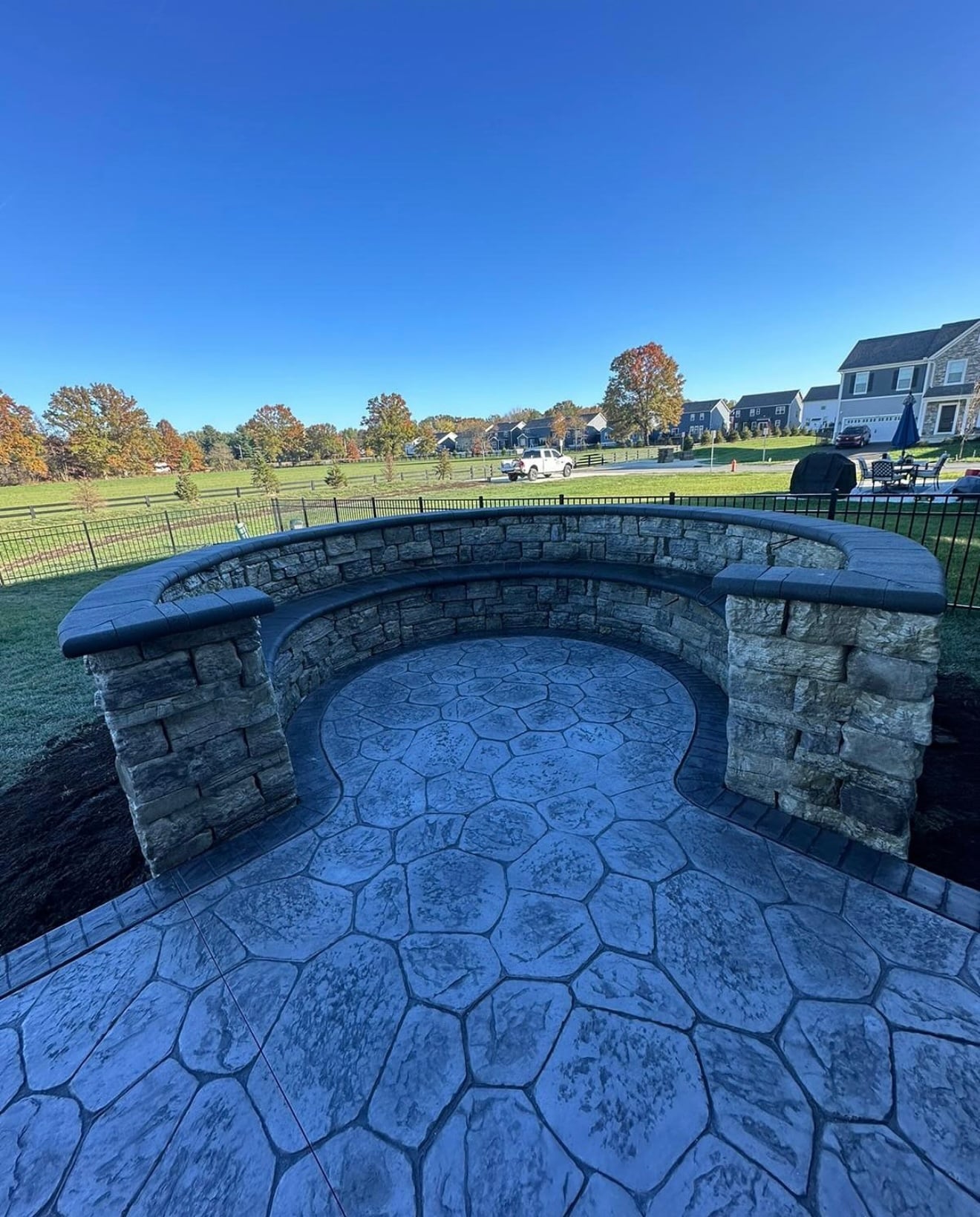 Curved stone seating wall around a circular blue-gray stamped patio in a suburban backyard.
