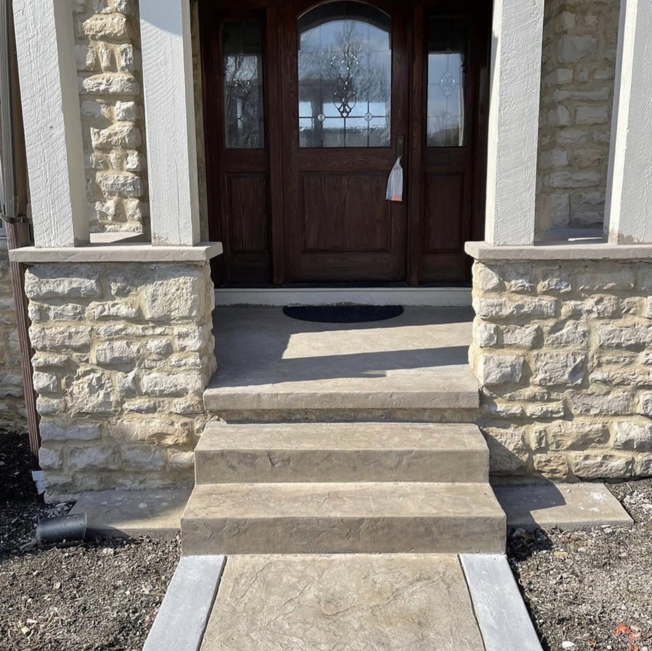 Stone-front porch with beige stone columns and a dark wood double door with decorative glass panels.