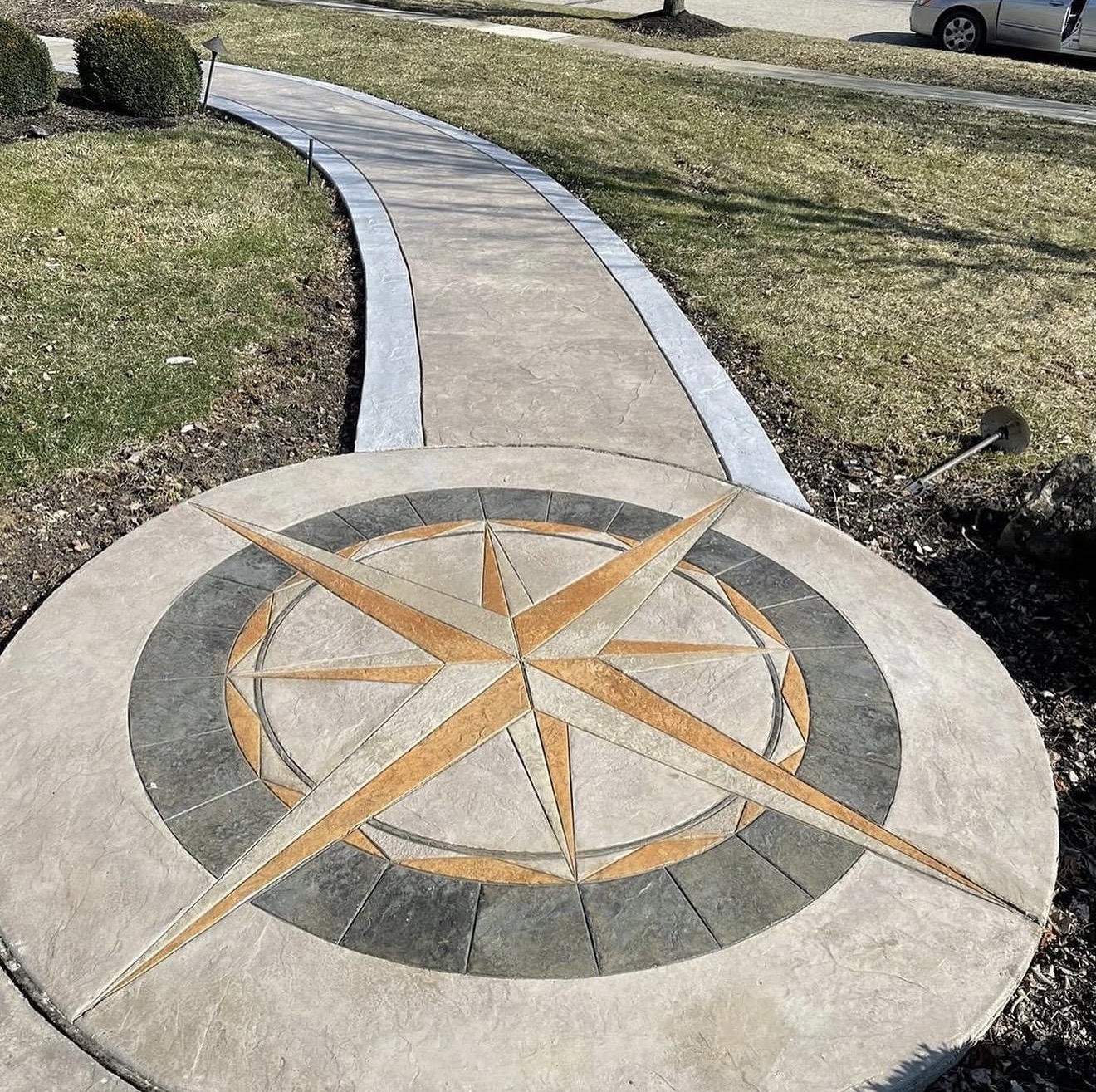 Circular compass rose inlay on concrete with orange and gray tiles, adjacent curved walkway in a park.