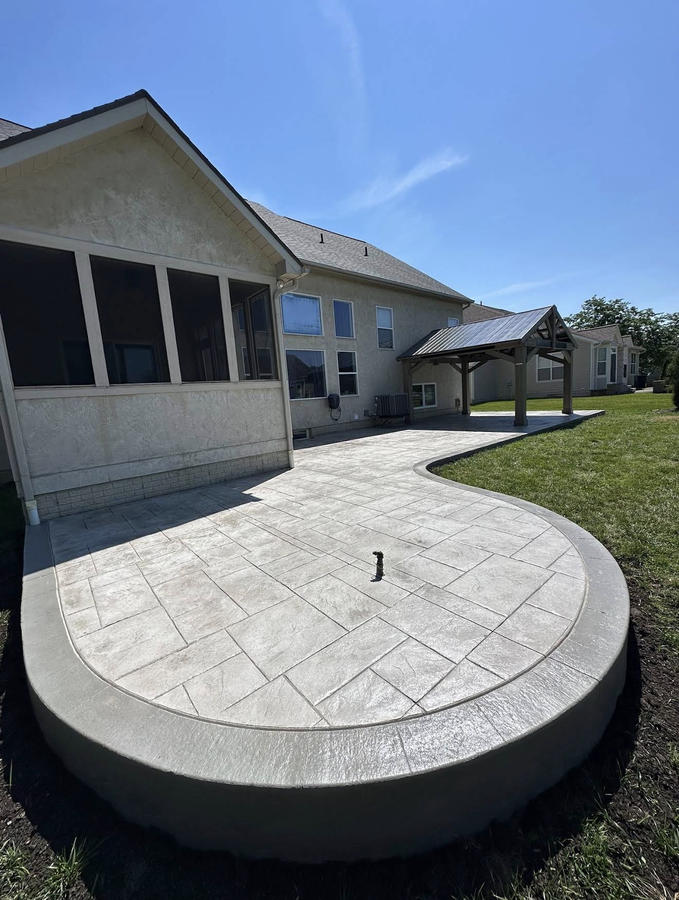 Circular stamped-concrete patio surrounding the house, with a screened porch on the left and a small wooden pergola in the yard.